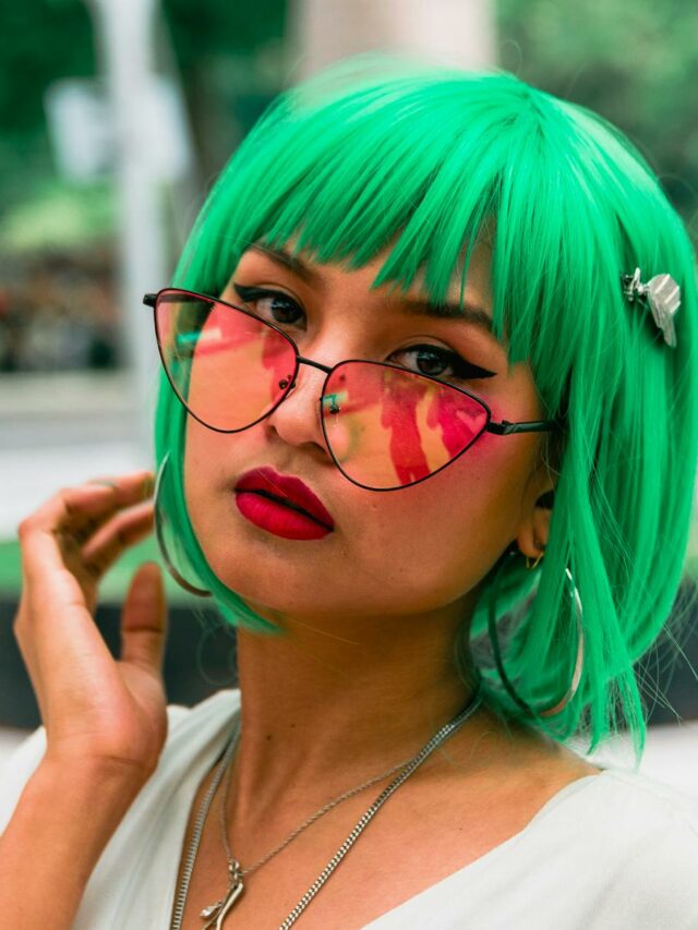 Colorful portrait capturing a stylish woman with bright green hair and reflective sunglasses.