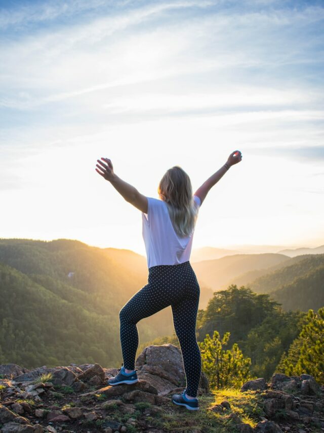 woman in white shirt and black pants standing on rocky mountain during daytime