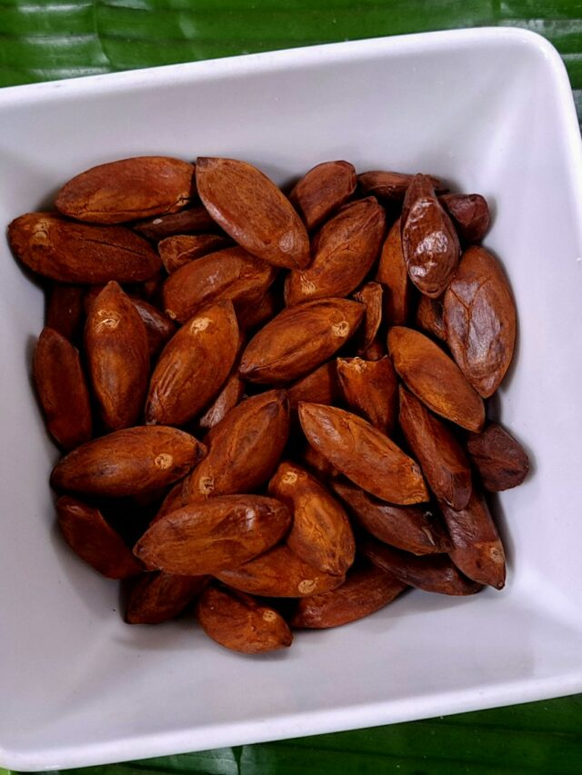 A white bowl filled with almonds on top of a green leaf