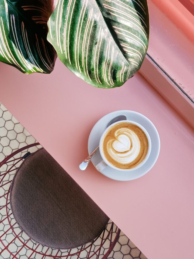 cup of coffee on saucer with teaspoon on pink tabletop